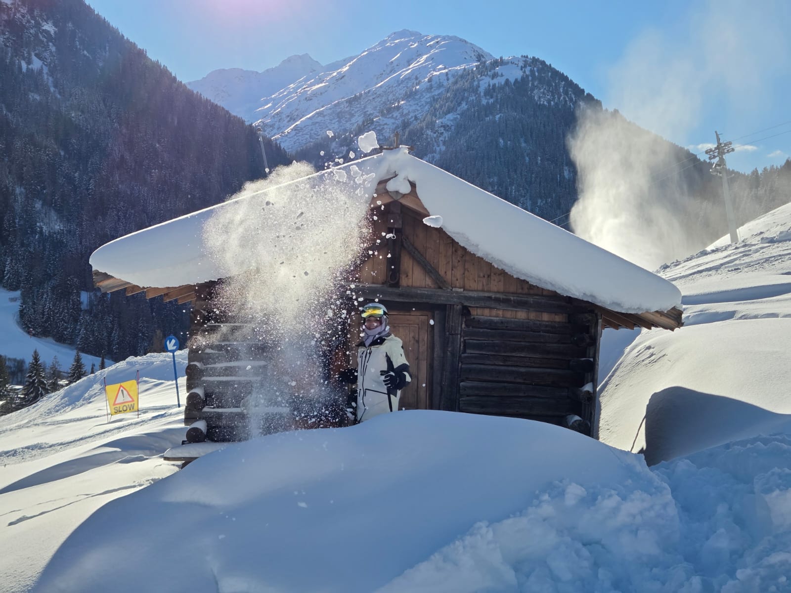 Person vor verschneiter Holzhütte in St. Anton am Arlberg mit frischem Pulverschnee und Bergpanorama